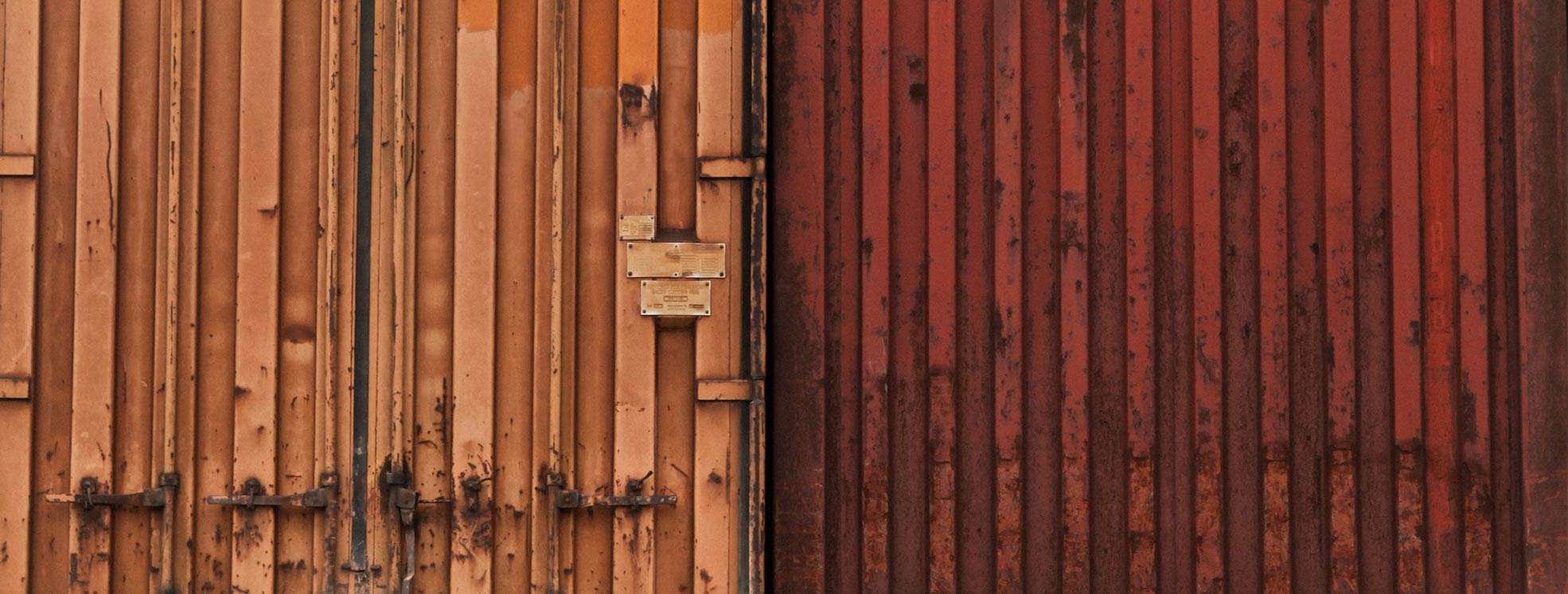 close up of two shipping container doors one is orange and one is maroon