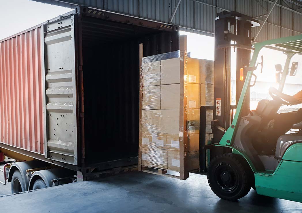 green forklift loading a pallet of boxes into a truck