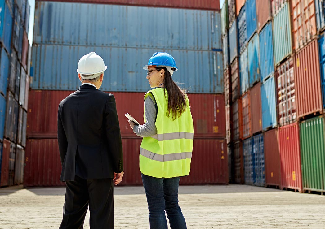 two people in hard hats talking near shipping containers